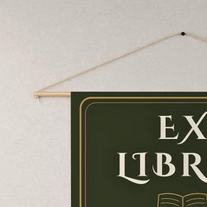 Peut inclure: Une banni&egrave;re murale rectangulaire vert fonc&eacute; avec le texte EX LIBRIS en police serif cr&egrave;me au-dessus d'une ic&ocirc;ne de livre ouvert stylis&eacute;e. La banni&egrave;re est suspendue &agrave; une tige en bois clair avec une fine ficelle beige pour la fixation.