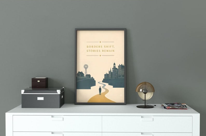 May include: A framed vertical poster featuring a cream-colored background with a dark blue silhouette of a town and a windmill. A winding yellow path leads to a lone figure standing in the center. The text reads: BORDERS SHIFT, STORIES REMAIN.