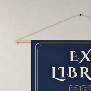 May include: A rectangular navy blue wall hanging banner featuring a gold border and the text EX LIBRIS in a cream-colored serif font. The banner is suspended from a light-colored wooden rod with a thin, natural-toned string attached for hanging.