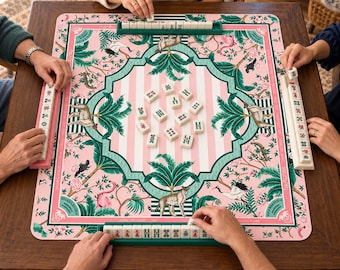 Peut inclure: Un tapis de jeu de mah-jong carré avec un centre rayé rose et blanc et une bordure décorative verte. Le tapis présente des illustrations de léopards, de flamants roses et de grues au milieu d'un feuillage tropical. Des tuiles sont disposées.