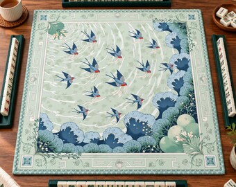 Può includere: Un tappetino da mahjong quadrato con sfondo verde chiaro, decorato con un motivo di rondini in volo e onde marine stilizzate blu scuro. Il tappetino è circondato da quattro rastrelliere verde scuro con tessere bianche con simboli rossi e verdi.