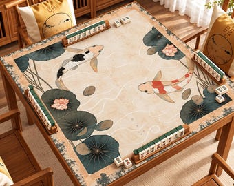 Può includere: Un tavolo da mahjong quadrato con un tappetino beige decorato con il disegno di due pesci koi che nuotano tra foglie di loto verde scuro e fiori rosa. Quattro supporti in legno sui bordi contengono file di tessere bianche da mahjong.