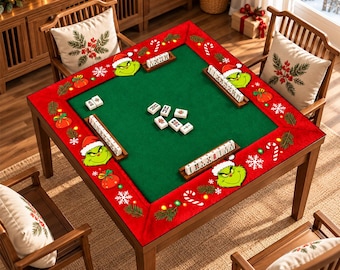 Può includere: Un tavolo da gioco quadrato in legno con una superficie in feltro verde e un bordo rosso decorato con volti del Grinch, bastoncini di zucchero e fiocchi di neve. Quattro supporti in legno contengono tessere bianche con segni neri.