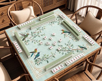 Può includere: Un tavolo da mahjong quadrato con una superficie verde chiaro decorata con illustrazioni di colibrì e rami fioriti. Il tavolo è allestito con file di tessere da mahjong verdi e bianche lungo i bordi e sparse al centro del piano.
