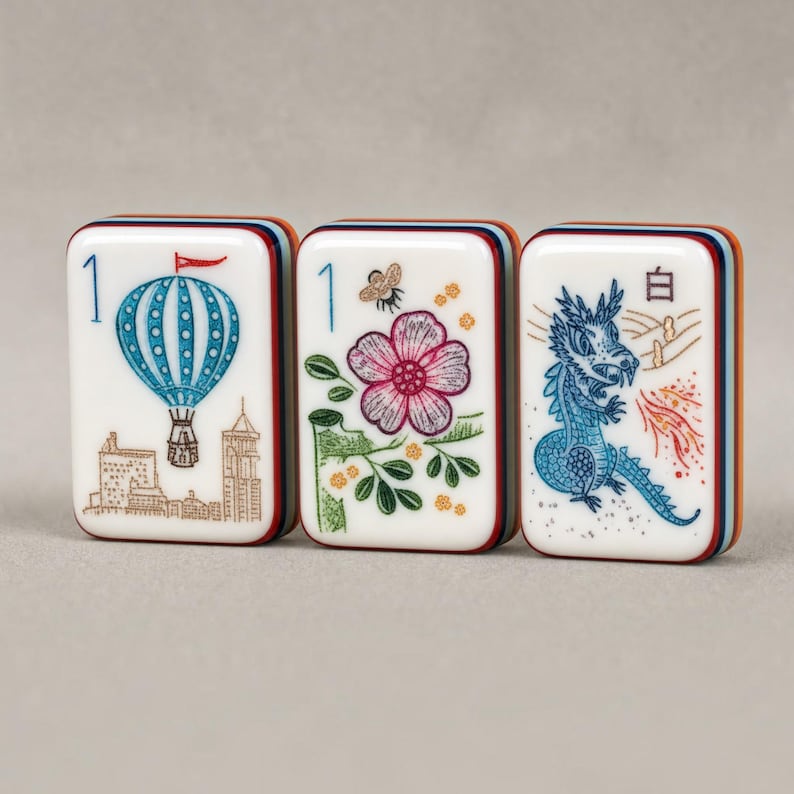 Puede incluir: Tres fichas de mahjong rectangulares con caras blancas y bordes de capas multicolores. La primera ficha presenta un globo aerost&aacute;tico azul y el n&uacute;mero 1. La segunda muestra una flor, una abeja y el n&uacute;mero 1. La tercera muestra un drag&oacute;n azul y el car&aacute;cter 白.