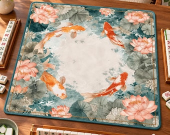 Può includere: Un tappetino quadrato per mahjong con un motivo stampato di pesci koi arancioni che nuotano tra fiori di loto rosa e foglie di ninfea verdi su uno sfondo chiaro, bordato da una sottile linea dorata e un bordo blu ottanio scuro.