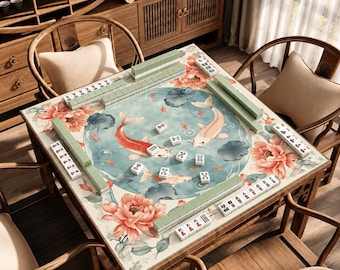 Può includere: Un tavolo da mahjong quadrato con una superficie decorata con l'illustrazione di uno stagno circolare contenente due pesci koi, circondato da grandi peonie rosa e foglie verdi, con tessere del mahjong disposte lungo i bordi.