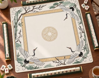 Può includere: Un tappetino da gioco per mahjong quadrato con un centro bianco e un motivo geometrico circolare dorato, circondato da un bordo di gru, bambù e fiori di prugno. Quattro rastrelliere verde scuro contengono tessere bianche da mahjong.