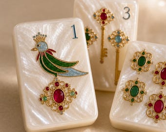 Puede incluir: Tres fichas rectangulares de color blanco perla. La primera ficha muestra un pájaro con corona y un colgante de piedra roja. La segunda muestra el número 3, una llave y una piedra azul. La tercera ficha presenta tres adornos con piedras.