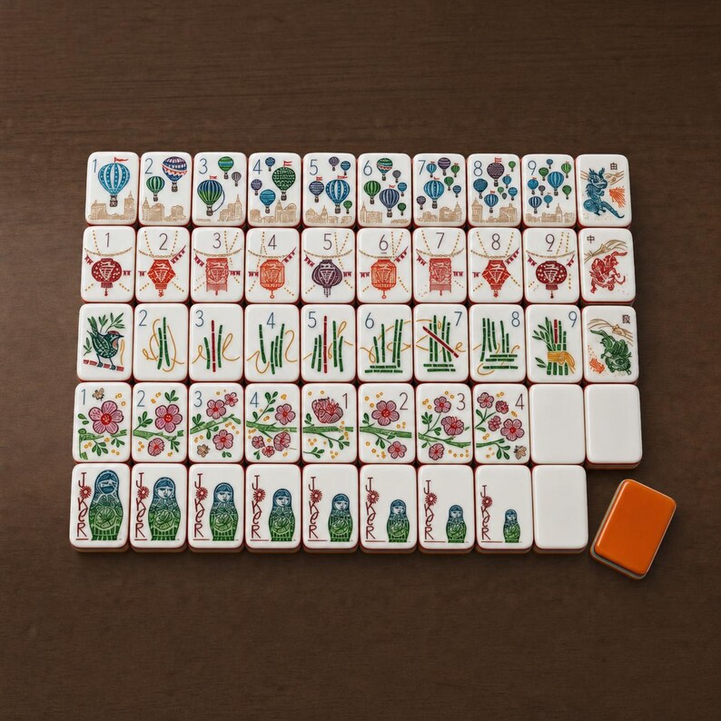 Puede incluir: Un conjunto de fichas de mahjong rectangulares dispuestas en cuadr&iacute;cula, con ilustraciones coloridas de globos aerost&aacute;ticos, linternas, tallos de bamb&uacute;, flores de cerezo y mu&ntilde;ecas rusas etiquetadas como Joker, con una ficha naranja lisa aparte.