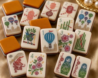 May include: A collection of rectangular mahjong tiles featuring cream-colored faces with colorful illustrations of hot air balloons, flowers, birds, dragons, lanterns, and nesting dolls, alongside solid orange-backed tiles and numbered markings.