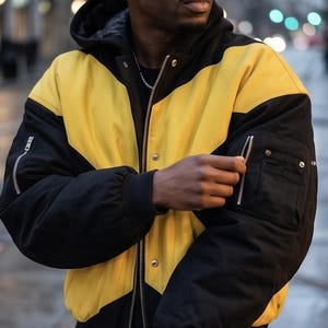 Peut inclure: Un blouson bomber noir et jaune à blocs de couleurs avec une capuche, une fermeture éclair frontale intégrale, des boutons-pression et une poche utilitaire zippée sur la manche. Le blouson présente des poignets côtelés et une coupe structurée.