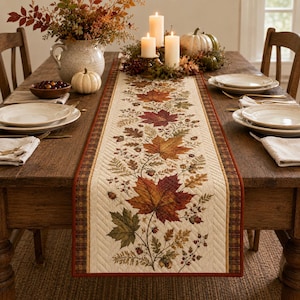 May include: A rectangular quilted table runner featuring a central print of colorful autumn maple leaves, acorns, and ferns on a cream background, bordered by a dark red and brown plaid pattern with intricate diagonal stitching along the edges.