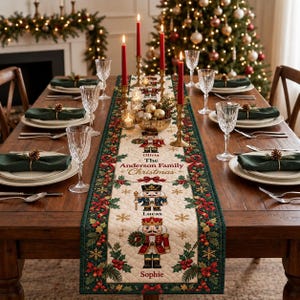 May include: A cream-colored quilted table runner featuring a festive border of green holly leaves, red berries, and ribbons. The center displays three illustrated nutcrackers and the text: Emma, Olivia, The Anderson Family Christmas, Lucas, Sophie.