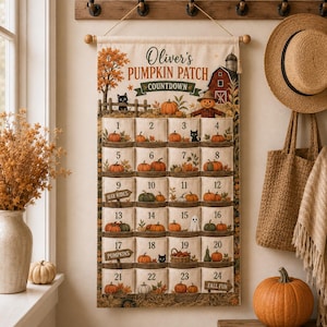 May include: A hanging fabric wall calendar titled Oliver's PUMPKIN PATCH COUNTDOWN, featuring twenty-four numbered pockets decorated with illustrations of pumpkins, black cats, a barn, and a ghost, suspended from a wooden rod with a rope.