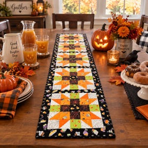 May include: A rectangular quilted table runner featuring a repeating star pattern in orange, lime green, white, and black. The fabric displays Halloween-themed prints including spider webs, candy corn, and ghosts, finished with a black border.