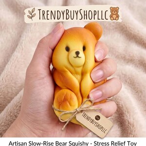 May include: A golden-yellow bear-shaped squishy stress relief toy with a smooth texture, small black eyes, and a simple nose. A small wooden tag tied with twine features the text TRENDYBUYSHOPLLC and the Etsy logo, with the shop name above.