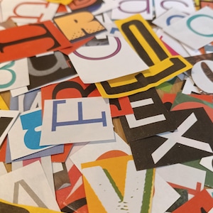 May include: A collection of assorted paper cutouts featuring various letters of the alphabet in different fonts, sizes, and colours including yellow, blue, red, black, and white. The paper pieces are scattered in an overlapping arrangement.