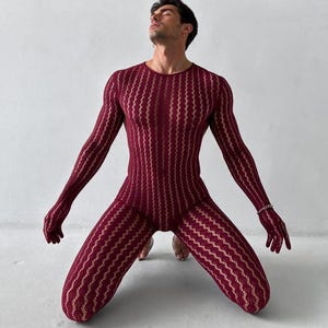 Op de afbeelding: Een bodysuit met lange mouwen en volledige lengte in een diepe bordeauxrode kleur, voorzien van een verticaal, golvend, semi-transparant kanten patroon. Het kledingstuk heeft geïntegreerde handschoenen en loopt door tot aan de voeten.