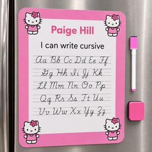 May include: A rectangular pink magnetic dry-erase board featuring Hello Kitty graphics in the corners. The board displays the text Paige Hill, I can write cursive, and the alphabet in cursive script. A pink-capped dry-erase marker is attached.