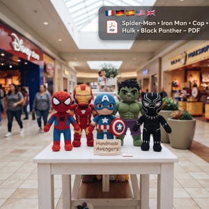 May include: Five crocheted dolls representing Spider-Man, Iron Man, Captain America with a shield, Hulk, and Black Panther stand on a white table. A small wooden sign in front reads "Handmade Avengers". A digital overlay lists the characters in PDF format.