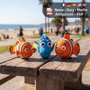 Könnte beinhalten: Drei gehäkelte Amigurumi-Fischspielzeuge, bestehend aus zwei orange-weißen Clownfischen und einem blau-schwarzen Doktorfisch. Der Text Nemo • Dory • Marlin Amigurumi – PDF steht oben im Bild und weist auf eine digitale Anleitung hin.