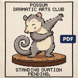 A finished possum dramatic arts club cross stitch piece, stitched and framed on a wall