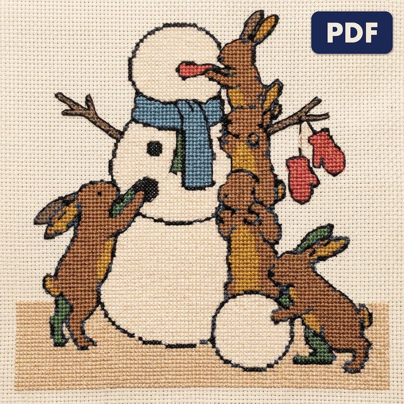 A finished rabbits building a snowman cross stitch piece, stitched and framed on a wall