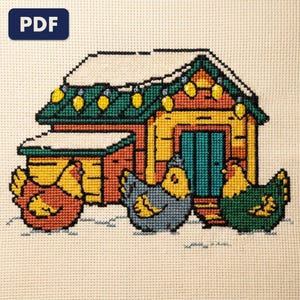 A finished hens before a winter coop cross stitch piece, stitched and framed on a wall