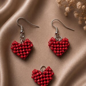 May include: A pair of drop earrings and a matching pendant, each featuring a heart-shaped charm crafted from small, vibrant red beads arranged in a grid pattern. The earrings include silver-toned metal hooks, while the pendant has a small loop.
