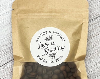 Peut inclure: Un sac en papier brun avec une fenêtre transparente remplie de grains de café. Un autocollant rond blanc avec du texte noir indique "Harriot & Michael Love is Brewing March 12, 2023".