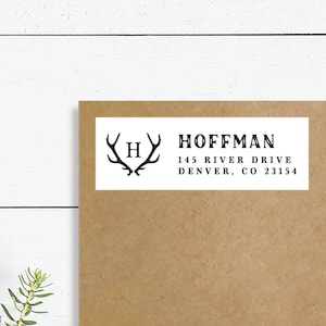 Könnte beinhalten: Ein weißes Rücksendeetikett mit einem schwarzen Hirschgeweih-Monogramm und dem Text "HOFFMAN", "145 RIVER DRIVE" und "DENVER, CO 23154".