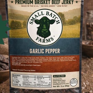 Könnte beinhalten: Ein beigefarbener und brauner Beutel mit Small Batch Farms Premium Brisket Beef Jerky in der Geschmacksrichtung Knoblauch-Pfeffer. Die Verpackung zeigt eine Kuh-Illustration, Nährwertangaben, ein Nettogewicht von 85g und die Zutatenliste.