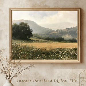 May include: A framed landscape painting depicting a golden field with white wildflowers in the foreground, dark green trees, and rolling hills under a soft, cloudy sky. The artwork is displayed in a light-colored wooden frame on a textured wall.