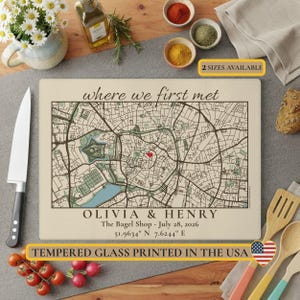 May include: A rectangular tempered glass cutting board featuring a printed map with a red heart icon, the text "where we first met", "OLIVIA & HENRY", "The Bagel Shop - July 28, 2026", and coordinates "51.9634 N 7.6244 E".