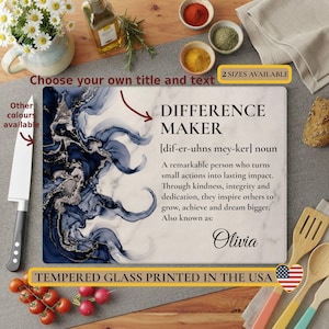 May include: A rectangular tempered glass cutting board featuring a white marble background with a navy blue and silver abstract ink swirl design. The text reads: DIFFERENCE MAKER [dif-er-uhns mey-ker] noun, followed by a definition and the name Olivia.