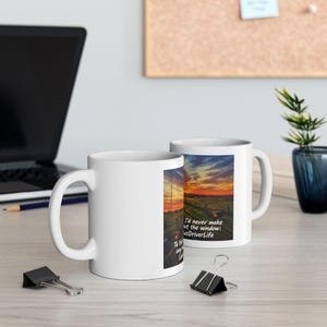 May include: Two white ceramic mugs featuring a printed graphic of a sunset over a rural landscape with a fence and the text: I'd never make it out the window: #BusDriverLife. The mugs have a standard handle and a smooth, glossy white finish.