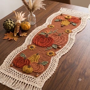 Könnte beinhalten: Ein rechteckiger Häkel-Tischläufer in Rostbraun mit applizierten Kürbissen, Zierkürbissen und Sonnenblumen. Der Läufer hat eine cremefarbene Häkelborte mit Fransen an beiden Enden. Der Text Harvest Hearth Designs ist auf dem Bild zu sehen.