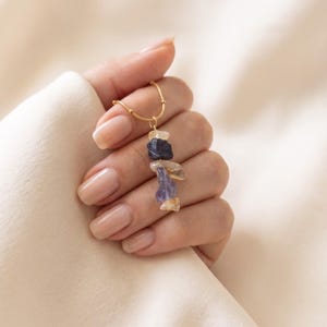 May include: A gold-toned chain necklace featuring a vertical pendant composed of five raw, irregularly shaped gemstone chips in shades of dark blue, light purple, and translucent yellow, suspended from a delicate metallic link chain.