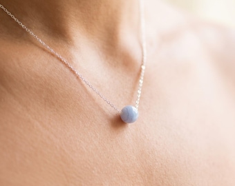 May include: A delicate silver chain necklace featuring a single, round, light blue lace agate bead pendant. The smooth, polished stone displays subtle, concentric white banding patterns, suspended centrally on a thin, metallic link chain.