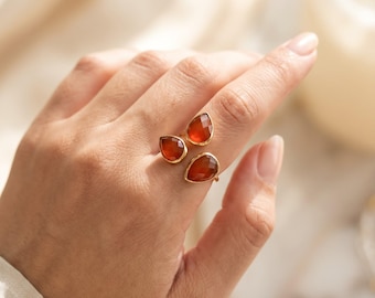 May include: A gold-toned open ring featuring three faceted, teardrop-shaped orange carnelian stones. The stones are arranged in a cluster, with two stones positioned on one side of the open band and one stone on the opposite side.