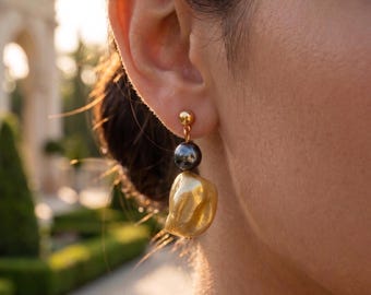 May include: A gold stud earring featuring a small gold sphere at the top, a dark grey spherical bead in the center, and a larger, irregular, textured gold drop pendant at the bottom, all suspended from a gold post and backing mechanism.