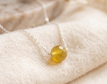 May include: A delicate silver chain necklace featuring a single, round, faceted yellow gemstone bead as the central pendant. The chain is thin and metallic, holding the translucent, golden-yellow stone securely in the middle of the strand.