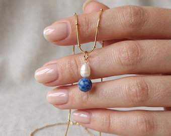 May include: A gold chain necklace featuring a delicate beaded texture along the links. The pendant consists of a single white oval freshwater pearl positioned directly above a round, mottled blue sodalite gemstone bead on a gold jump ring.