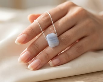 May include: A necklace featuring a polished, rectangular light blue agate pendant with subtle white banding, suspended from a delicate silver chain. The stone has a smooth, faceted surface and is centered on the thin metallic link chain.