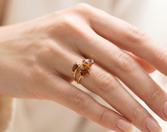 May include: A gold ring featuring two raw, amber-colored gemstones set on a thin, polished gold band. The stones have an irregular, jagged texture and are positioned at the top of the ring, creating a distinct, open-ended design on the finger.