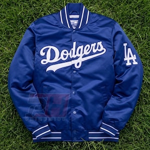 Può includere: Una giacca varsity in raso blu reale con il logo Dodgers in corsivo bianco sul petto e il logo LA intrecciato bianco sulla manica sinistra. La giacca presenta una chiusura frontale con bottoni a pressione e colletto e polsini a coste a righe.