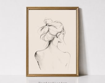 May include: A framed wall art print featuring a black ink line drawing of a person from the back, showing shoulders and a messy bun hairstyle. The artwork is set against a cream-colored background and enclosed in a thin gold-toned frame.