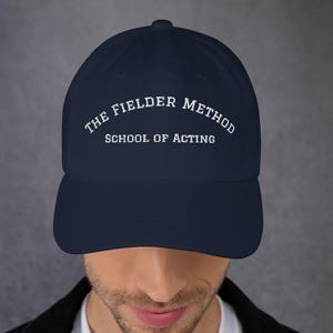 May include: Navy blue baseball cap with the text "THE FIELDER METHOD SCHOOL OF ACTING" in white lettering. The cap has a curved brim and a classic six-panel design. The hat is made of a soft, durable fabric.