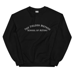 May include: Black sweatshirt with the text "THE FIELDER METHOD SCHOOL OF ACTING" in white, arched across the chest. The sweatshirt is a solid black color and appears to be made of a soft material. The Gildan logo is visible on the upper back.
